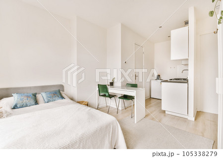 a bedroom with a bed, desk and small kitchen in the room next to the bed is a white refrigerator 105338279