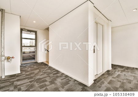 an empty office space with white walls and grey carpeting, there is a door leading to the left side an empty office space with white walls and grey carpeting, there is a door leading to the left side 105338409