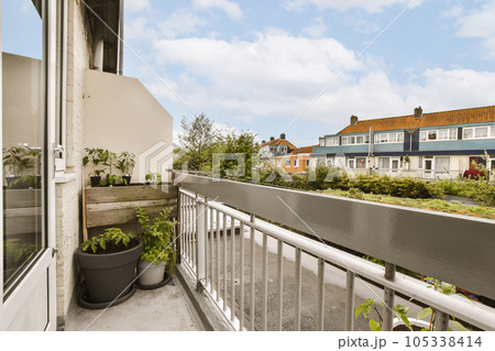 a balcony with potted plants on the railings and houses in the background, taken from an apartment window 105338414