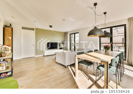 a living room with wood flooring and white walls, there is a dining table in front of the window 105338416