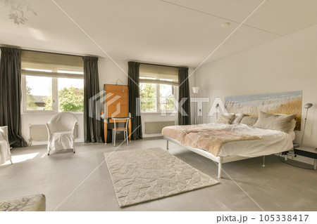 a bedroom with a bed, chair and desk in the middle of the room on the right is a large window 105338417