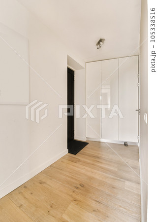 an empty room with white walls and wood flooring on the right, there is a black door to the left 105338516