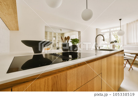 a modern kitchen with wood cabinets and white countertops in the center of the room is a large black bowl on the island 105338519