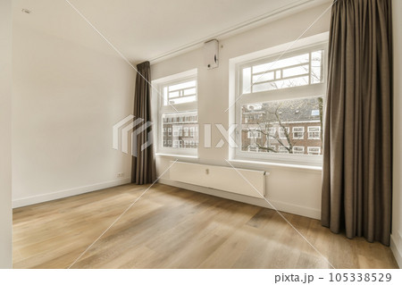 an empty living room with wood flooring and large windows in the photo is taken from the inside to the outside 105338529