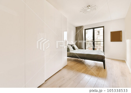 a bedroom with white walls and wood flooring, including a bed in the middle part of the room there is a large window 105338533