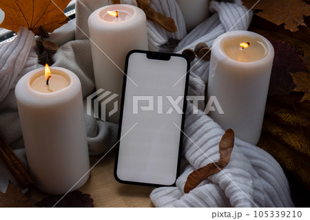 White screen mobile phone app copy space on background of aesthetic atmosphere Autumn leaves spices and candle on knitted white sweater in warm yellow lights. Still life. Raining 105339210