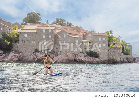 Young women Having Fun Stand Up Paddling in blue water sea near st stefan island in Montenegro. SUP Young women Having Fun Stand Up Paddling in blue water sea near st stefan island in Montenegro. SUP 105340614