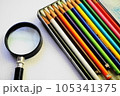 白い用紙の上に置かれた、カラフルな色鉛筆と虫眼鏡 105341375