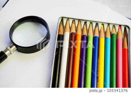 白い用紙の上に置かれた、カラフルな色鉛筆と虫眼鏡 105341376