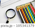 白い用紙の上に置かれた、カラフルな色鉛筆と虫眼鏡と定規 105341379