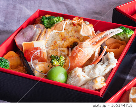 日本のお節料理。お正月の伝統料理。蟹の甲羅グラタンや鴨肉ハム、ドライトマトなどが入った重箱。 日本のお節料理。お正月の伝統料理。蟹の甲羅グラタンや鴨肉ハム、ドライトマトなどが入った重箱。 105344719