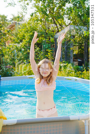 Cute teenage girl in pink swimsuit playing in a small pool.  105347531