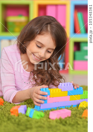 Portrait of cute girl playing with colorful plastic blocks in room 105348361