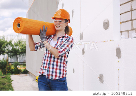 The woman with rolls of reinforcing fiberglass. Insulation of the house with polyfoam board on the facade 105349213