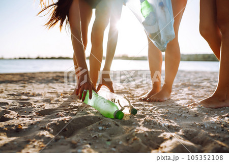 Three young girls pick up trash on the beach. Environmental pollution. Ecological problem. 105352108