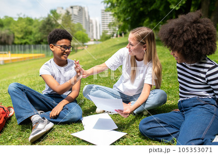 Blonde volunteer sitting on the grass and helping kids with tests Blonde volunteer sitting on the grass and helping kids with tests 105353071