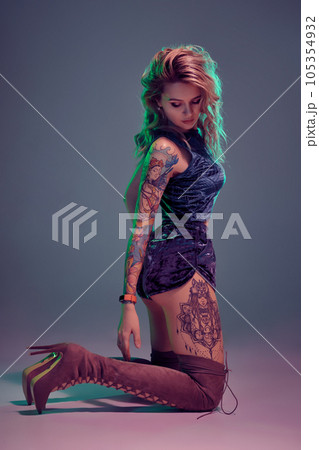 Attractive young blonde girl in blue velour booty shorts and maroon suede high boots posing on camera in studio Attractive young blonde girl in blue velour booty shorts and maroon suede high boots posing on camera in studio 105354932