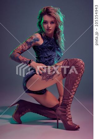 Attractive young blonde girl in blue velour booty shorts and maroon suede high boots posing on camera in studio Attractive young blonde girl in blue velour booty shorts and maroon suede high boots posing on camera in studio 105354943