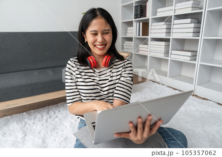 Cute teen woman asian is doing using laptop at home on the floor. She is excited and smiling Cute teen woman asian is doing using laptop at home on the floor. She is excited and smiling 105357062