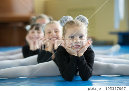 Little girls gymnasts sit on the splits. Children do physical exercise. Young ballerinas.. Training of the initial group on gymnastics.Acrobatics lesson Little girls gymnasts sit on the splits. Children do physical exercise. Young ballerinas.. Training of the initial group on gymnastics.Acrobatics lesson 105357067