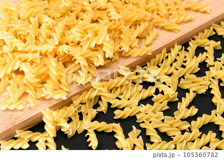 Uncooked Fusilli Pasta Scattered on Wooden Board 105360782