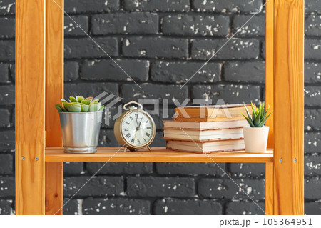 Wooden bookshelf with books and stuff against black brick wall 105364951