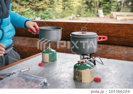 Tourist setting up pot on burner with canned gas in campground 105366289