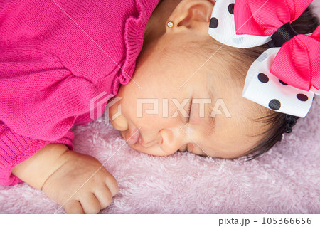 Closeup of a sweet little one month baby sleeping dressed in pink wearing a bow 105366656