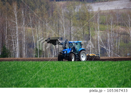 春の畑で畑を耕すトラクター 105367433