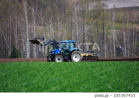 春の畑で畑を耕すトラクター 105367435