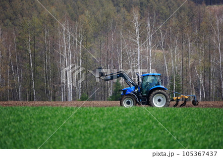 春の畑で畑を耕すトラクター 105367437