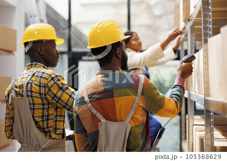 Shipment department workers using barcode scanner in warehouse. African american logistics managers scanning cardboard boxes and analyzing freight storing in industrial storehouse Shipment department workers using barcode scanner in warehouse. African american logistics managers scanning cardboard boxes and analyzing freight storing in industrial storehouse 105368629