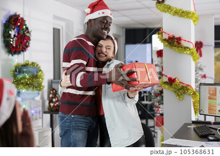 Excited employee receives special red box gift from african american coworker on Christmas season. Happy worker surprised with present during secret santa office party Excited employee receives special red box gift from african american coworker on Christmas season. Happy worker surprised with present during secret santa office party 105368631