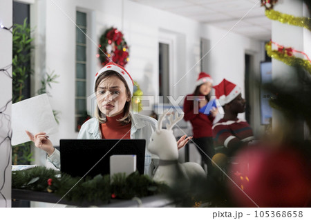 Unhappy overworked employee stressed by demanding paperwork during Christmas holiday season. Frustrated businesswoman overwhelmed by looming project deadline in festive decorated office Unhappy overworked employee stressed by demanding paperwork during Christmas holiday season. Frustrated businesswoman overwhelmed by looming project deadline in festive decorated office 105368658