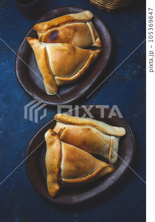 Tipical Chilean baked empanadas de pino y napolitano on clay plates with wine. Dish and drink on 18 September party Independence day Chile, blue background. Tipical Chilean baked empanadas de pino y napolitano on clay plates with wine. Dish and drink on 18 September party Independence day Chile, blue background. 105369647