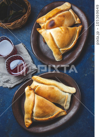Tipical Chilean baked empanadas de pino y napolitano on clay plates with wine. Dish and drink on 18 September party Independence day Chile, blue background. Tipical Chilean baked empanadas de pino y napolitano on clay plates with wine. Dish and drink on 18 September party Independence day Chile, blue background. 105369649