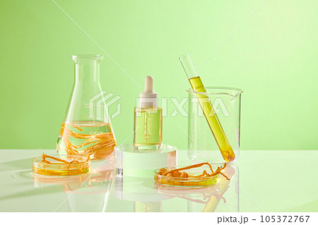 Against the green background, glass flask containing cordyceps and yellow liquid decorated with a serum bottle unbranded. Mockup scene for advertising cosmetic of cordyceps extract Against the green background, glass flask containing cordyceps and yellow liquid decorated with a serum bottle unbranded. Mockup scene for advertising cosmetic of cordyceps extract 105372767