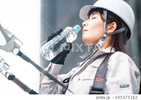 高所で水分補給をする若い女性職人 高所で水分補給をする若い女性職人 105373102