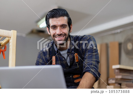 young carpenter caucasian man with laptop make drawing on wood to design at workspace. young carpenter caucasian man with laptop make drawing on wood to design at workspace. 105373888