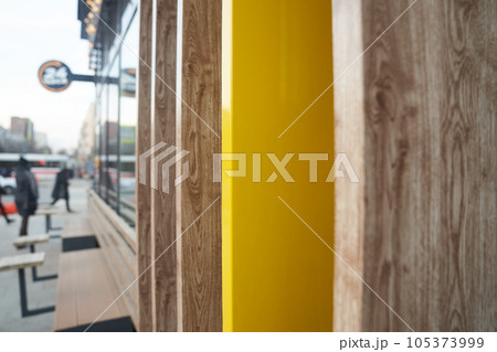 A fragment of a wall at the intersection of several natural-colored boards, a view of the street along the wall. Unrecognizable people near the cafe. High quality photo 105373999