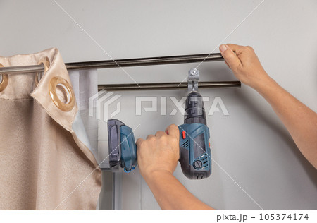 Worker repairman hanging and fixing the curtain on the window 105374174