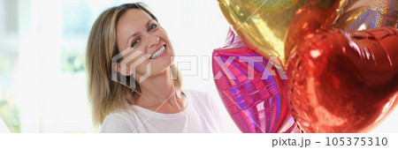 Pleased blonde woman smiling and holding many air baloons in hand. Pleased blonde woman smiling and holding many air baloons in hand. 105375310