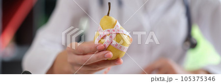 Nutritionist holds pear fruit and measuring tape in his hand and advises to eat healthy food with vitamins. Nutritionist holds pear fruit and measuring tape in his hand and advises to eat healthy food with vitamins. 105375346