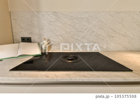 a white marble counter top with a black burner and an open book on the side, next to it a white marble counter top with a black burner and an open book on the side, next to it 105375508