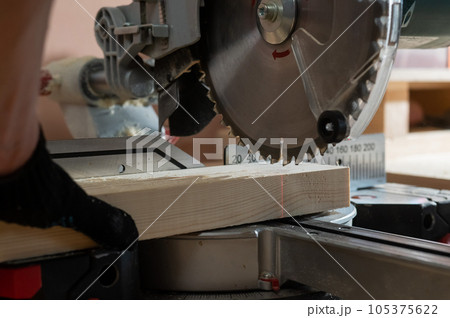 The master cuts the board with a circular saw in the workshop. Close-up of a carpenter's male hands at work. 105375622