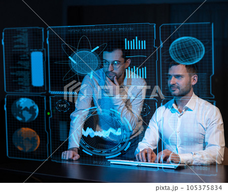 Two caucasian bearded men look in the dark at a virtual screen.  105375834