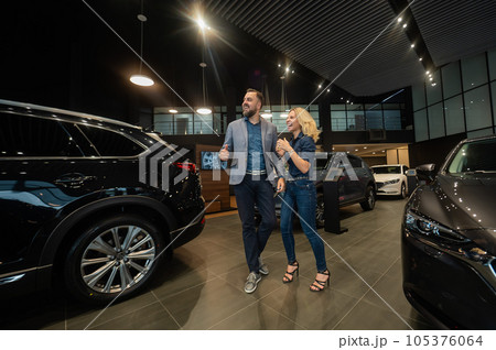 Happy married couple celebrating buying a car in a car showroom. 105376064