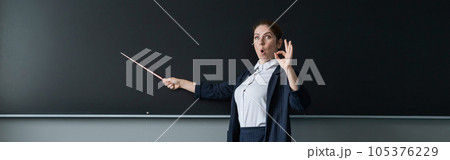 Red-haired caucasian woman in a pantsuit shows an ok sign. Surprised female teacher with a pointer at the blackboard. Widescreen. Red-haired caucasian woman in a pantsuit shows an ok sign. Surprised female teacher with a pointer at the blackboard. Widescreen. 105376229