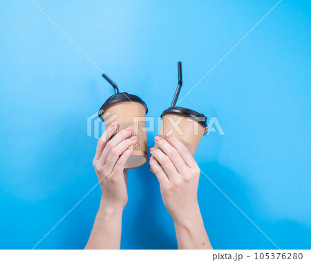 A woman holds two cardboard cups with coffee on a blue background. 105376280