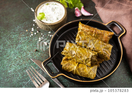 Traditional Greek, Caucasian and Turkish cuisine. Delicious dolma - stuffed grape leaves with rice and meat on a dark stone background. Copy space. Traditional Greek, Caucasian and Turkish cuisine. Delicious dolma - stuffed grape leaves with rice and meat on a dark stone background. Copy space. 105378283